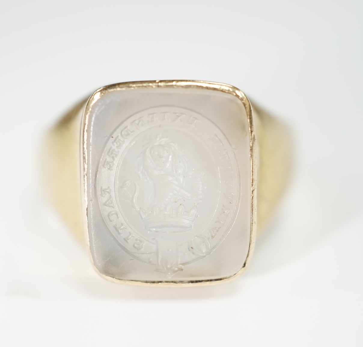 An early 20th century yellow metal and white chalcedony intaglio ring, the matrix carved with the motto 'Virtutum Extendere Factis' with crest, size W, gross weight 9.4 grams.